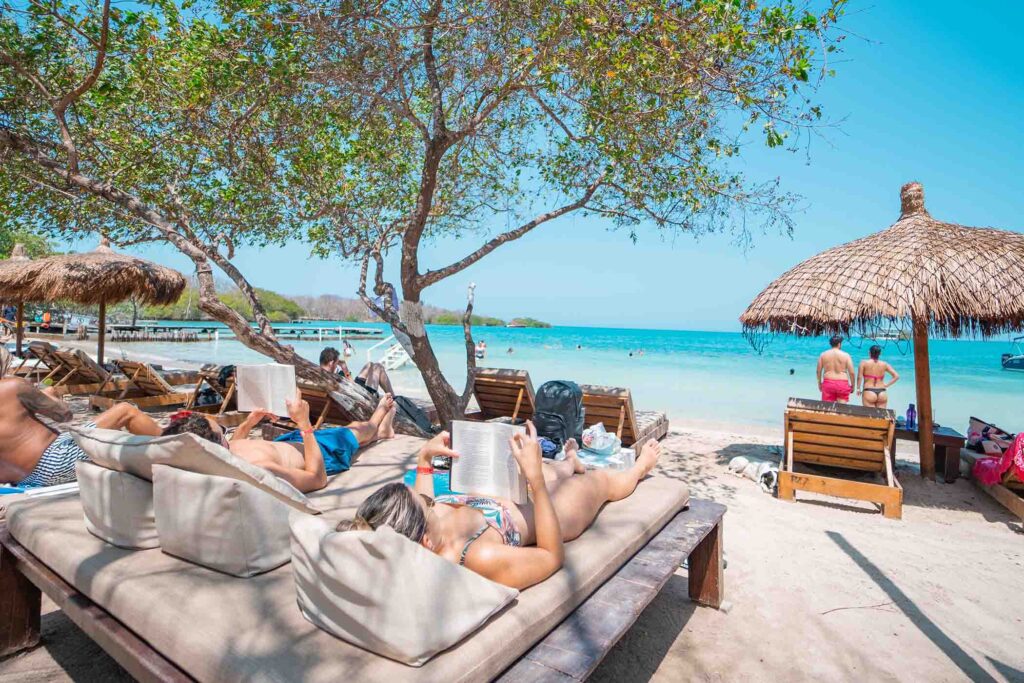 tranquil white sand beach with people lounging on beds and turquoise waters in the background